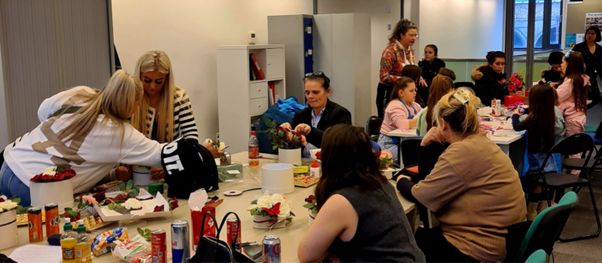 A group of people sitting across two tables engaged in a floral arrangement activity.