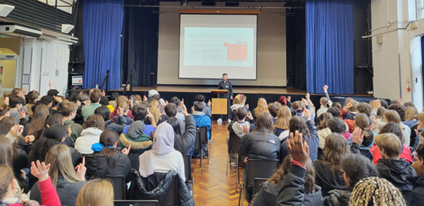 A hall full of students watching a political literacy being delivered.