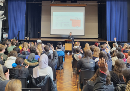 A hall full of students watching a political literacy being delivered.